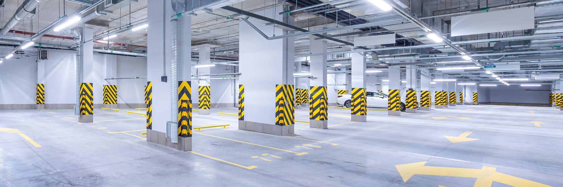 An empty parking garage with white columns, yellow arrows, and black and yellow striped posts.