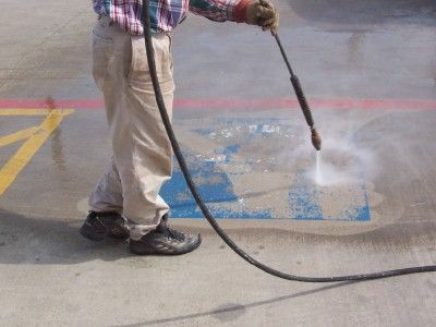 Person power washing blue painted markings on a concrete surface outside.