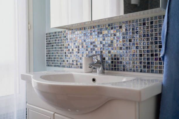 A bathroom sink with a mosaic tile wall behind it.