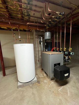A basement utility room featuring a residential boiler and a hot water storage tank with extensive overhead copper piping.