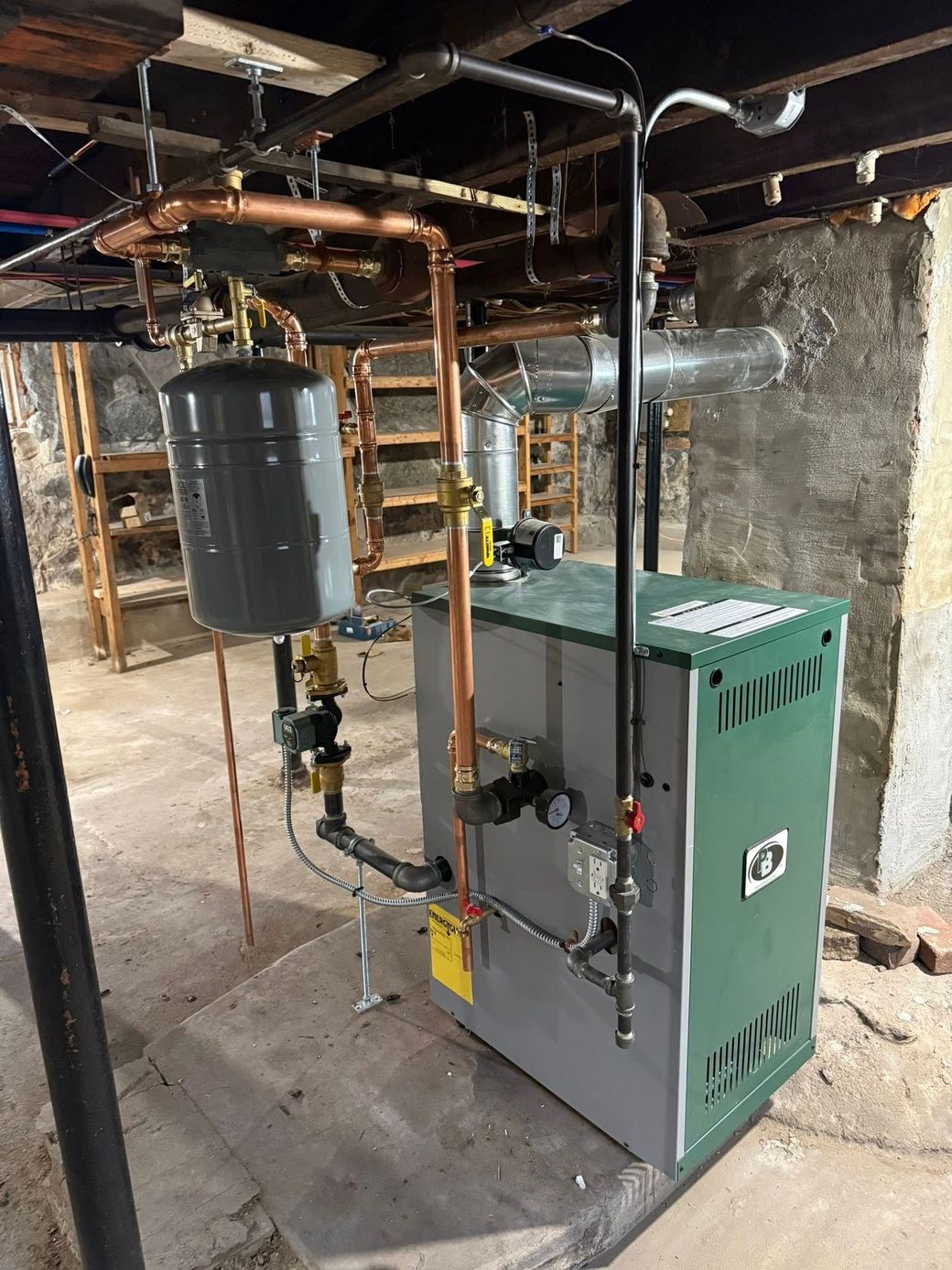 A green cast-iron boiler with copper piping and a grey expansion tank, installed in a basement.