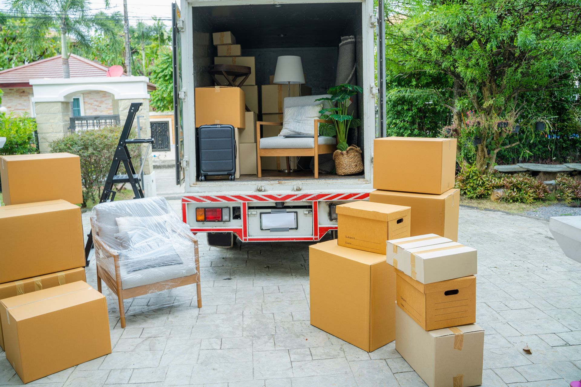 A moving truck parked in a driveway with its back open, surrounded by cardboard boxes.