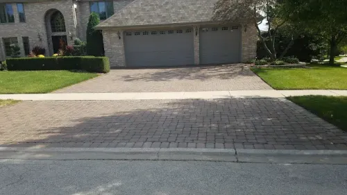 A suburban house with a brick paver driveway and sidewalk, viewed from the street.
