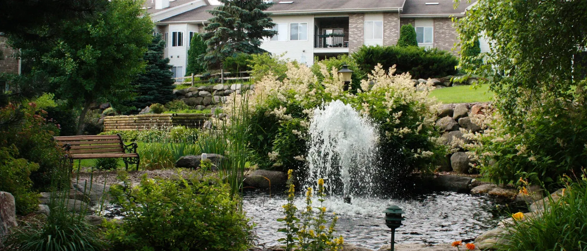 A fountain in a garden with a house in the background.