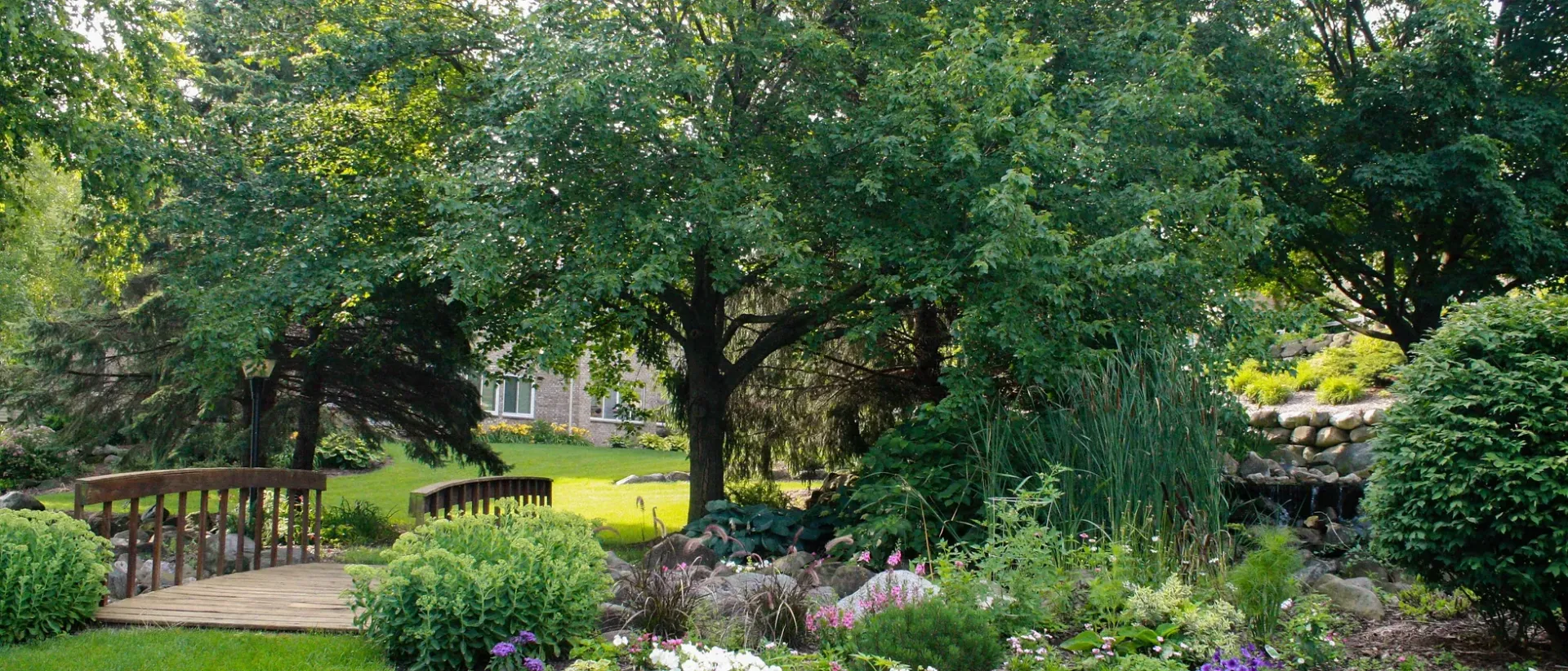 There is a bridge in the middle of a garden surrounded by trees.