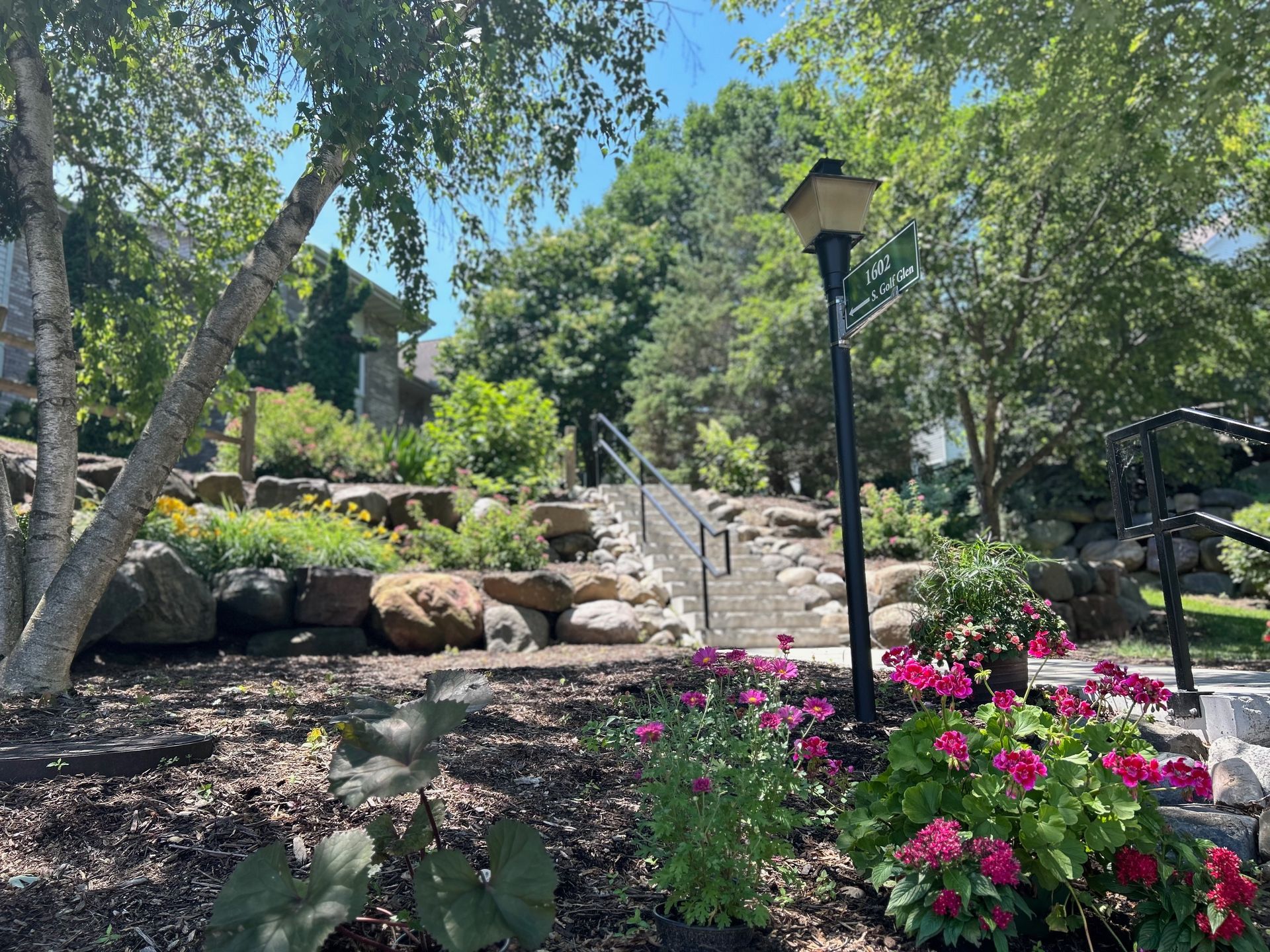 A park with stairs leading up to a house and flowers in the foreground.