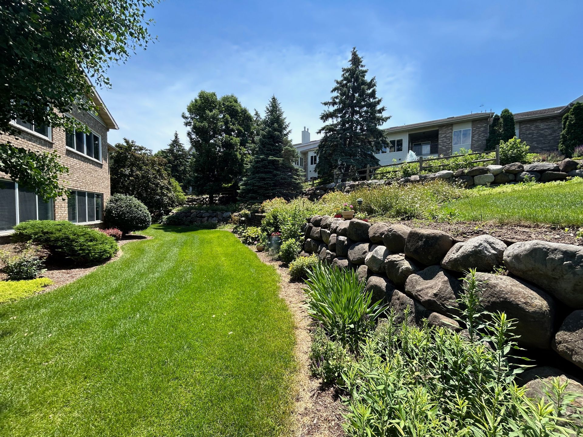 A house with a large lawn and a stone wall in front of it.