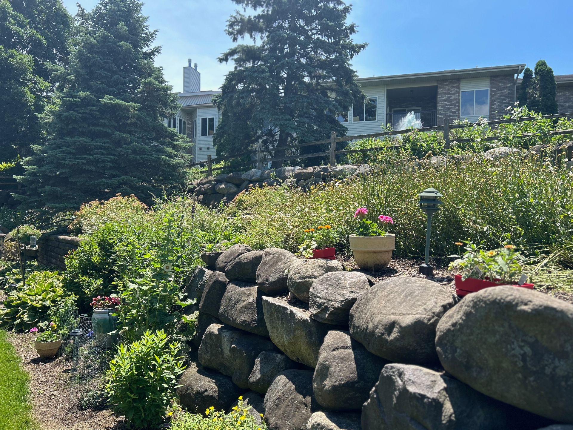 A large rock wall in a garden with a house in the background