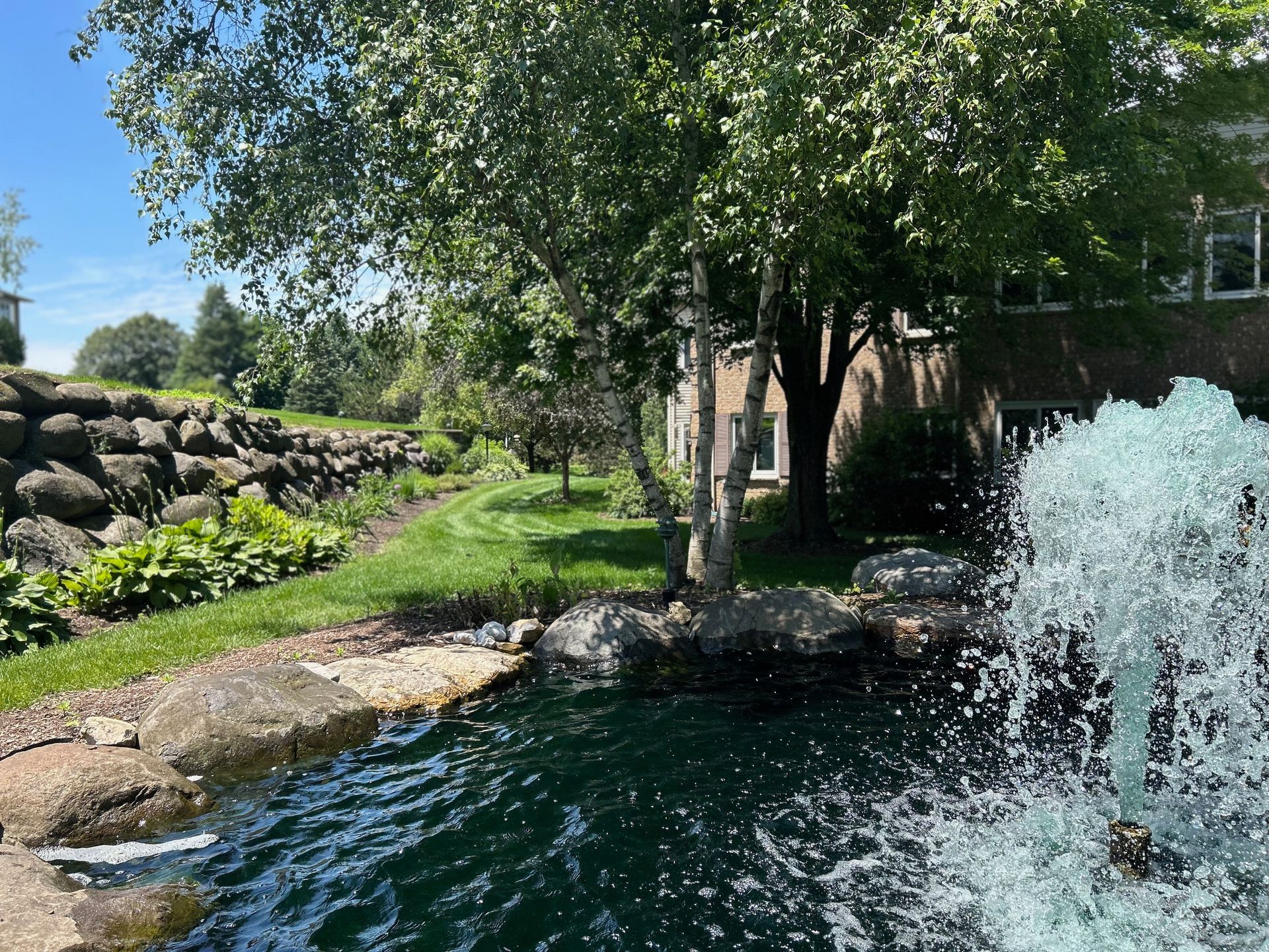 A fountain is spraying water into a pond in front of a house.