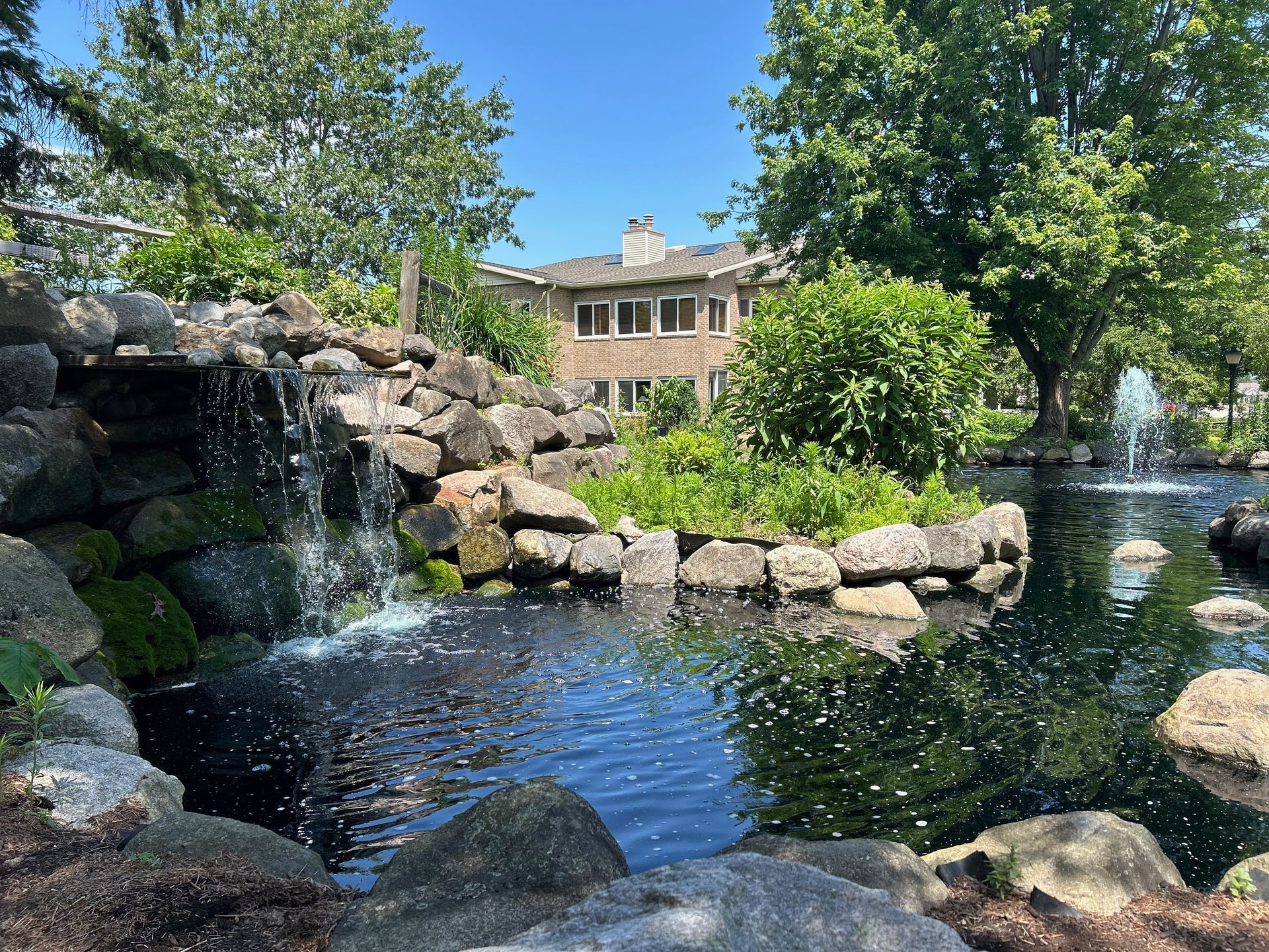 There is a waterfall in the middle of a pond in front of a house.