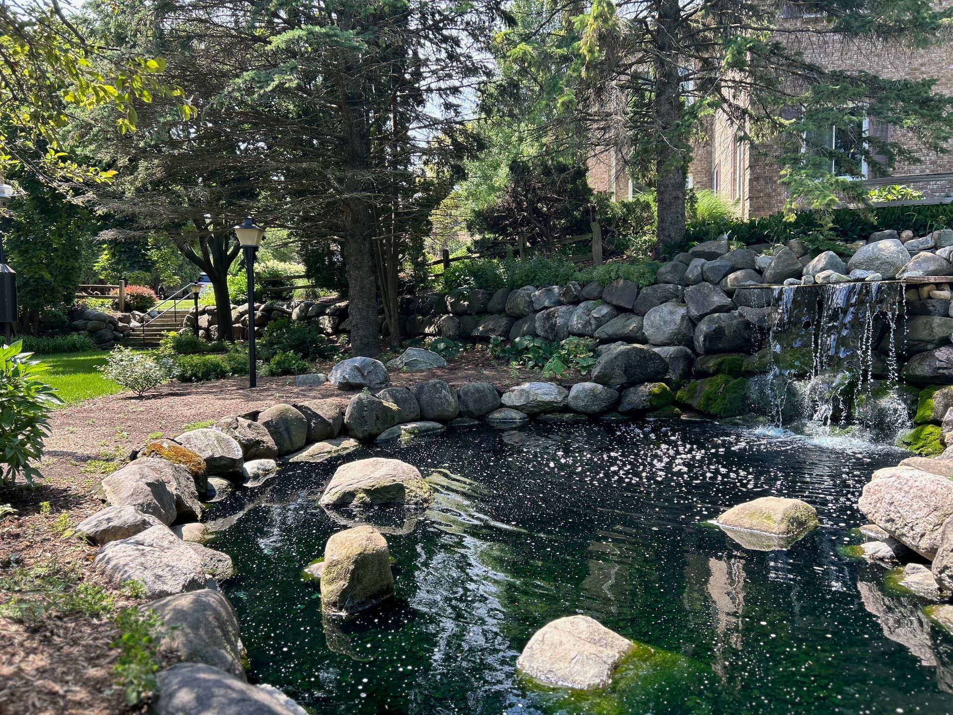 A pond surrounded by rocks and trees with a waterfall in the background.