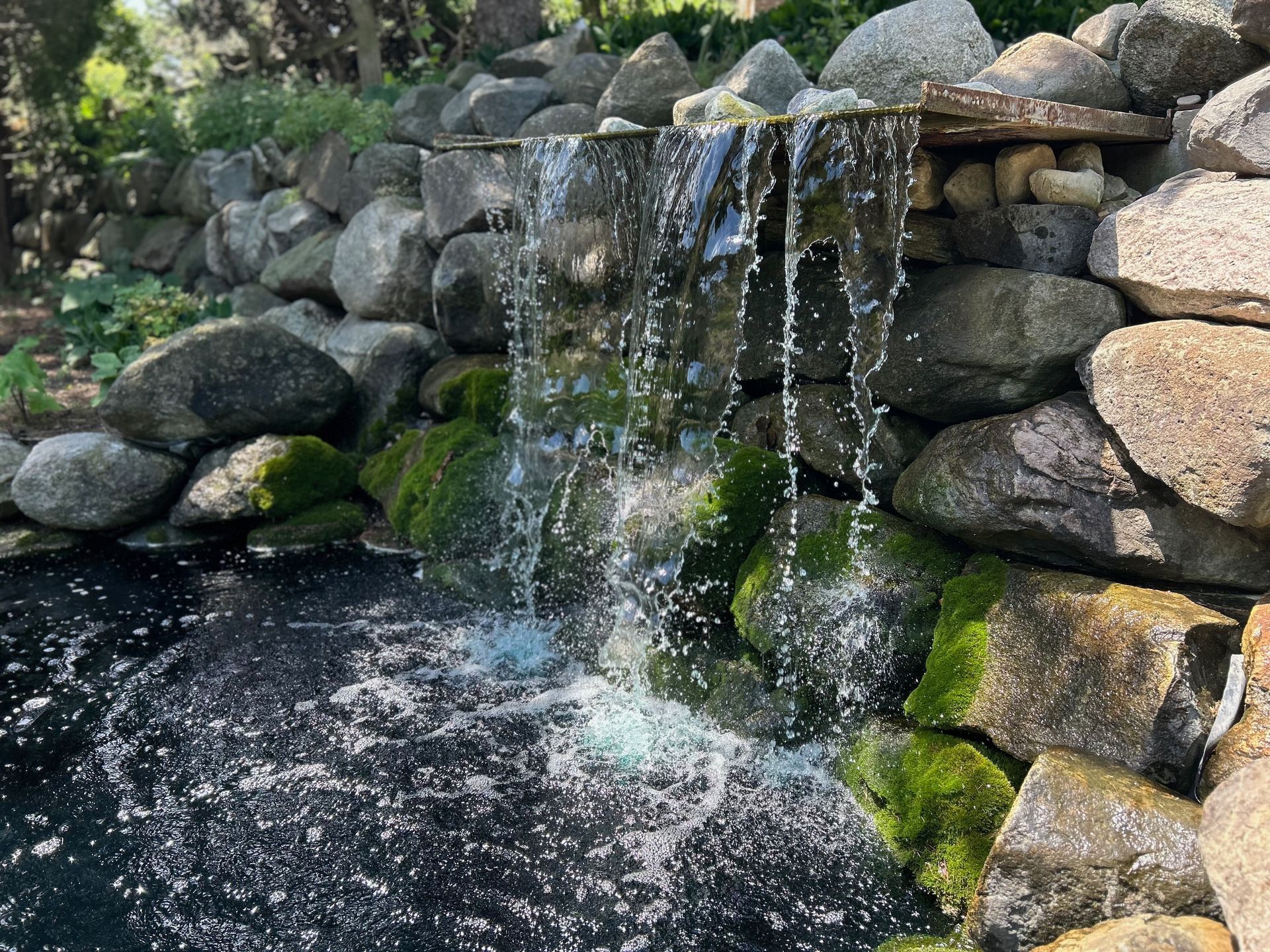 A waterfall is surrounded by rocks and moss in a pond.