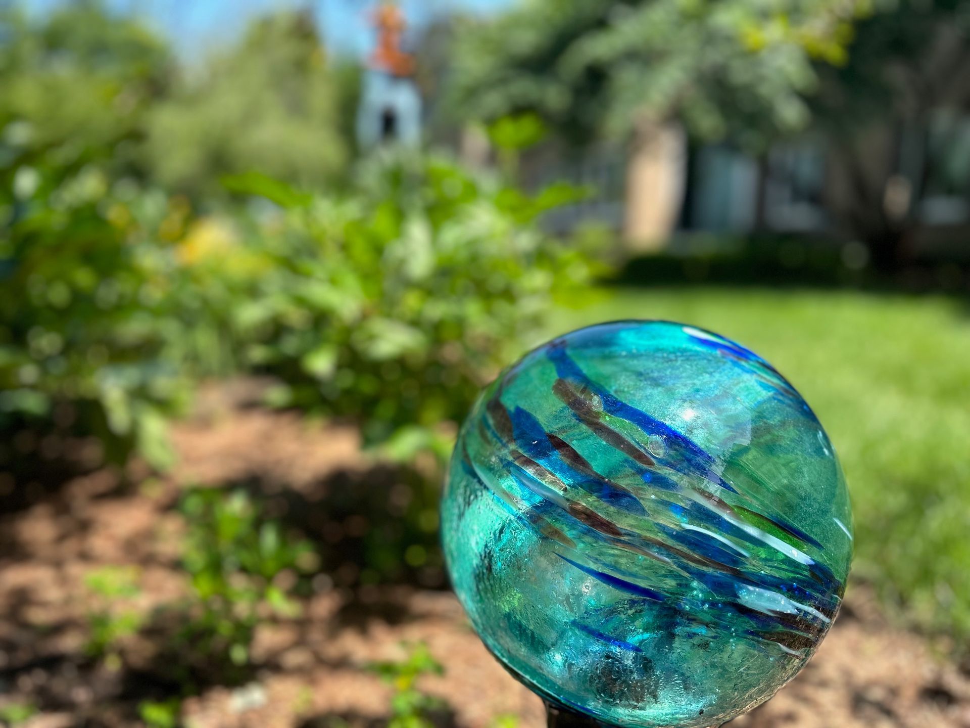 A blue glass ball is sitting on a pole in a garden.