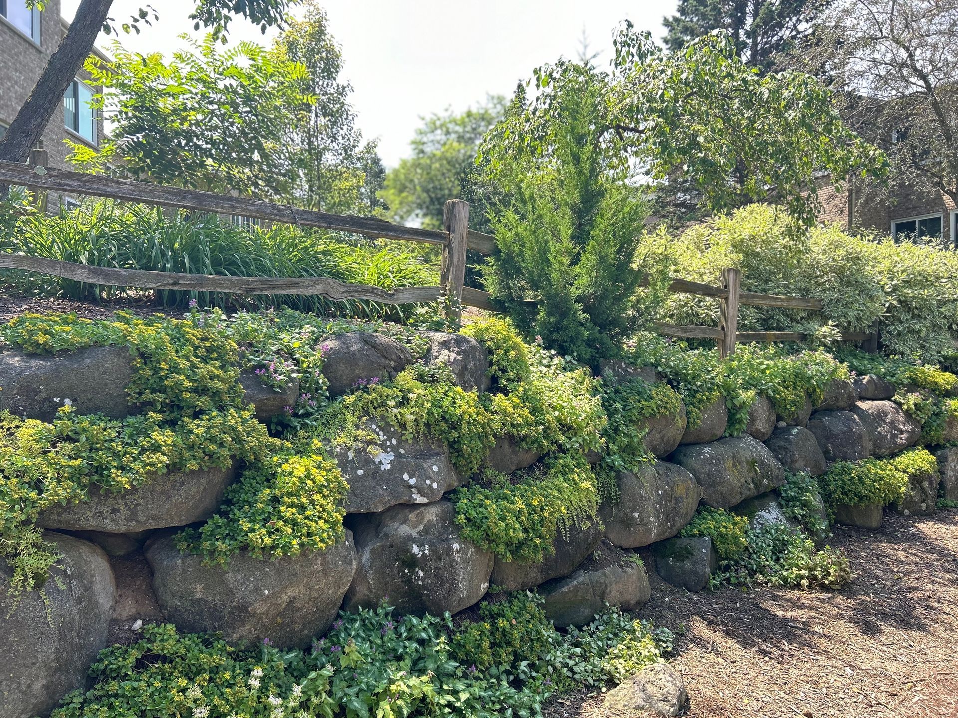 A wooden fence surrounds a rock wall in a garden.
