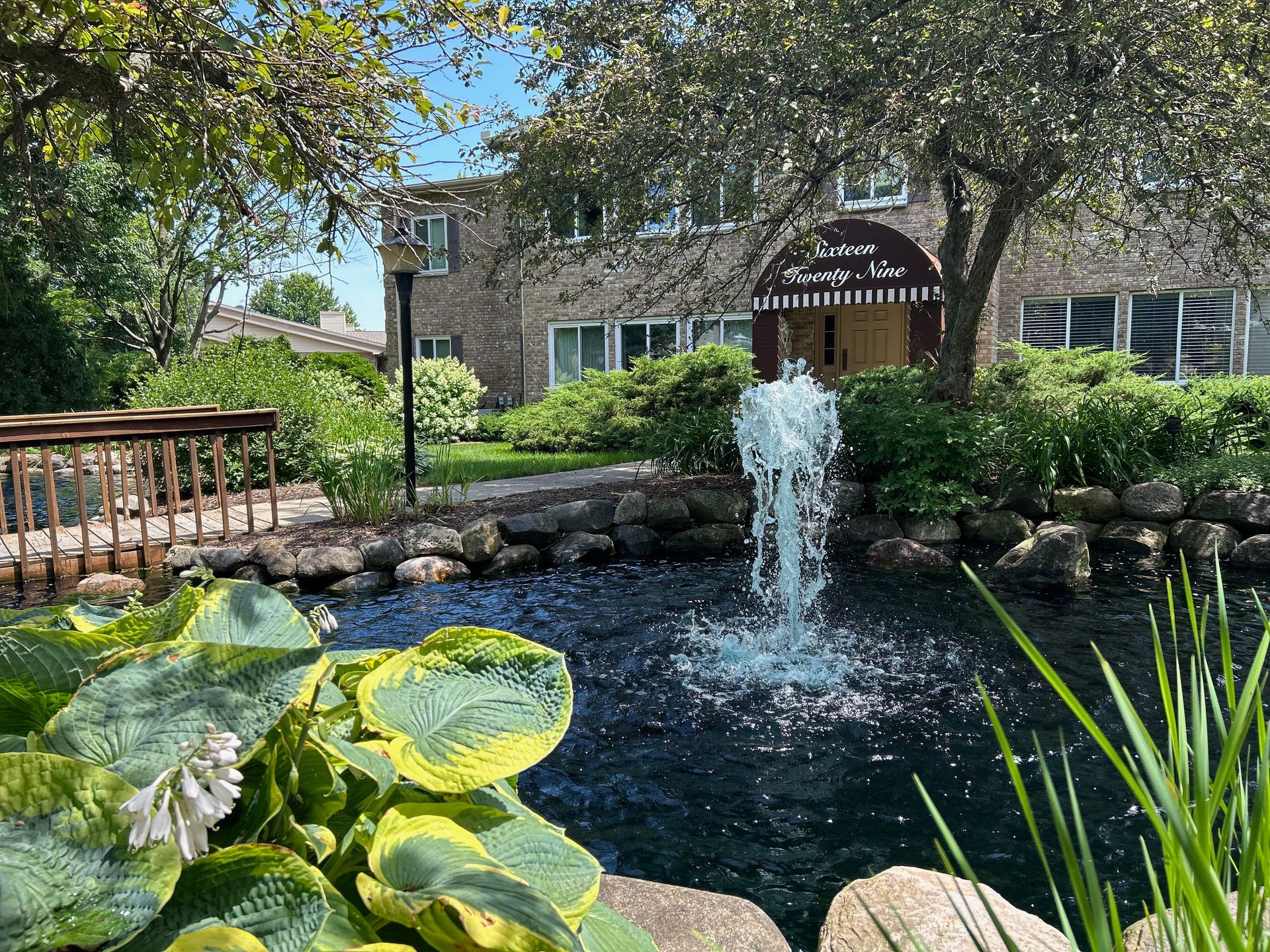 There is a fountain in the middle of a pond in front of a building.
