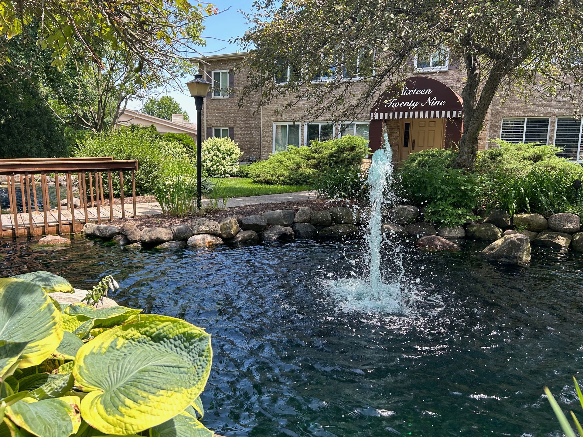 There is a fountain in the middle of a pond in front of a building.