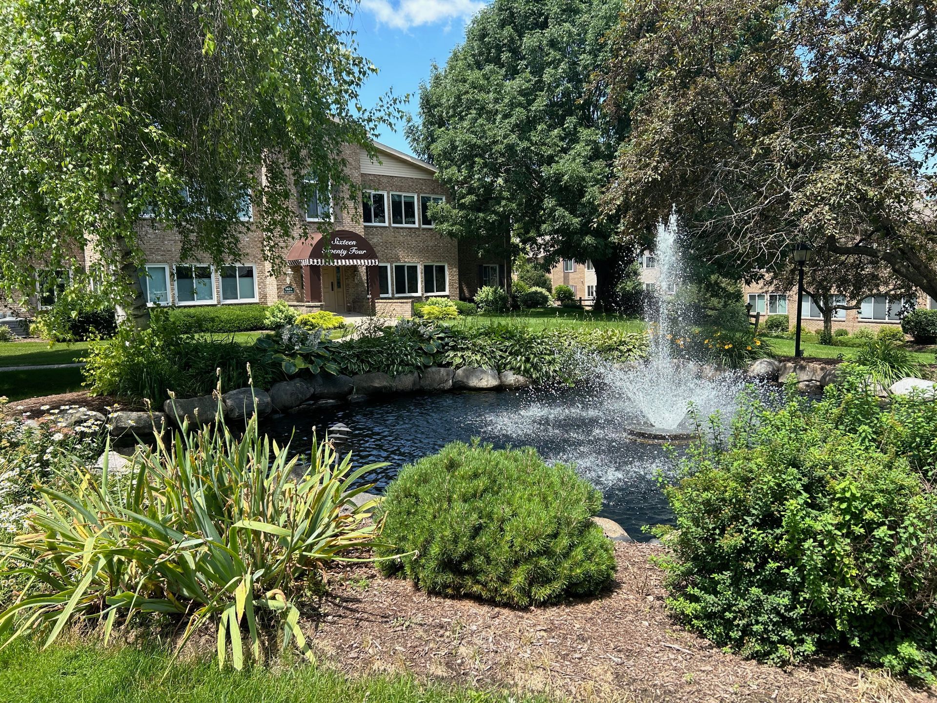 There is a fountain in the middle of a garden in front of a building.