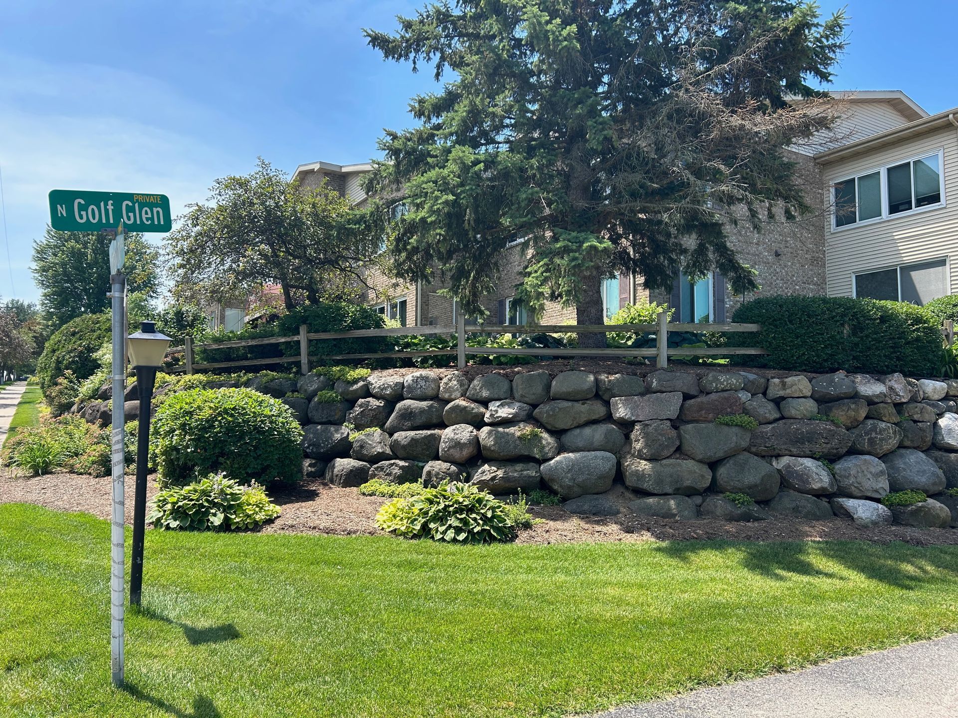 A stone wall is surrounded by grass and trees in front of a building.