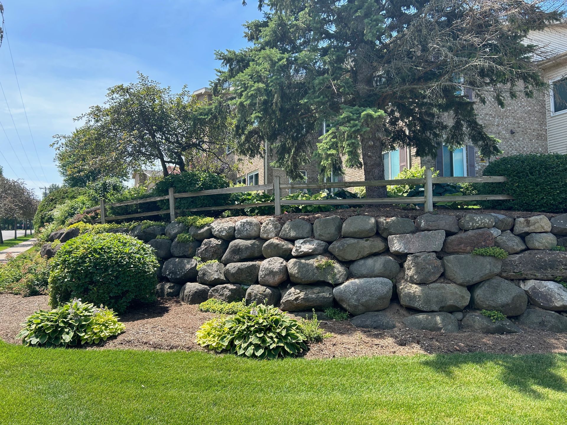 A large rock wall with a wooden fence in front of a house.