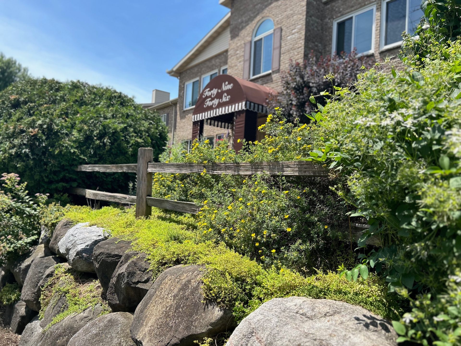 A large house with a red awning is surrounded by trees and rocks.
