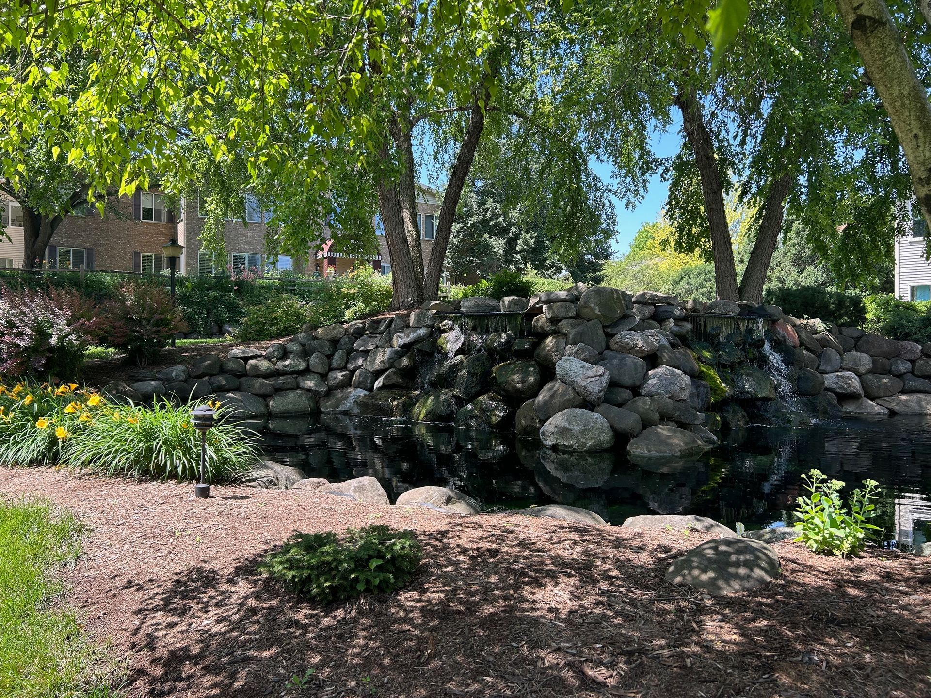 There is a waterfall in the middle of a park surrounded by trees.