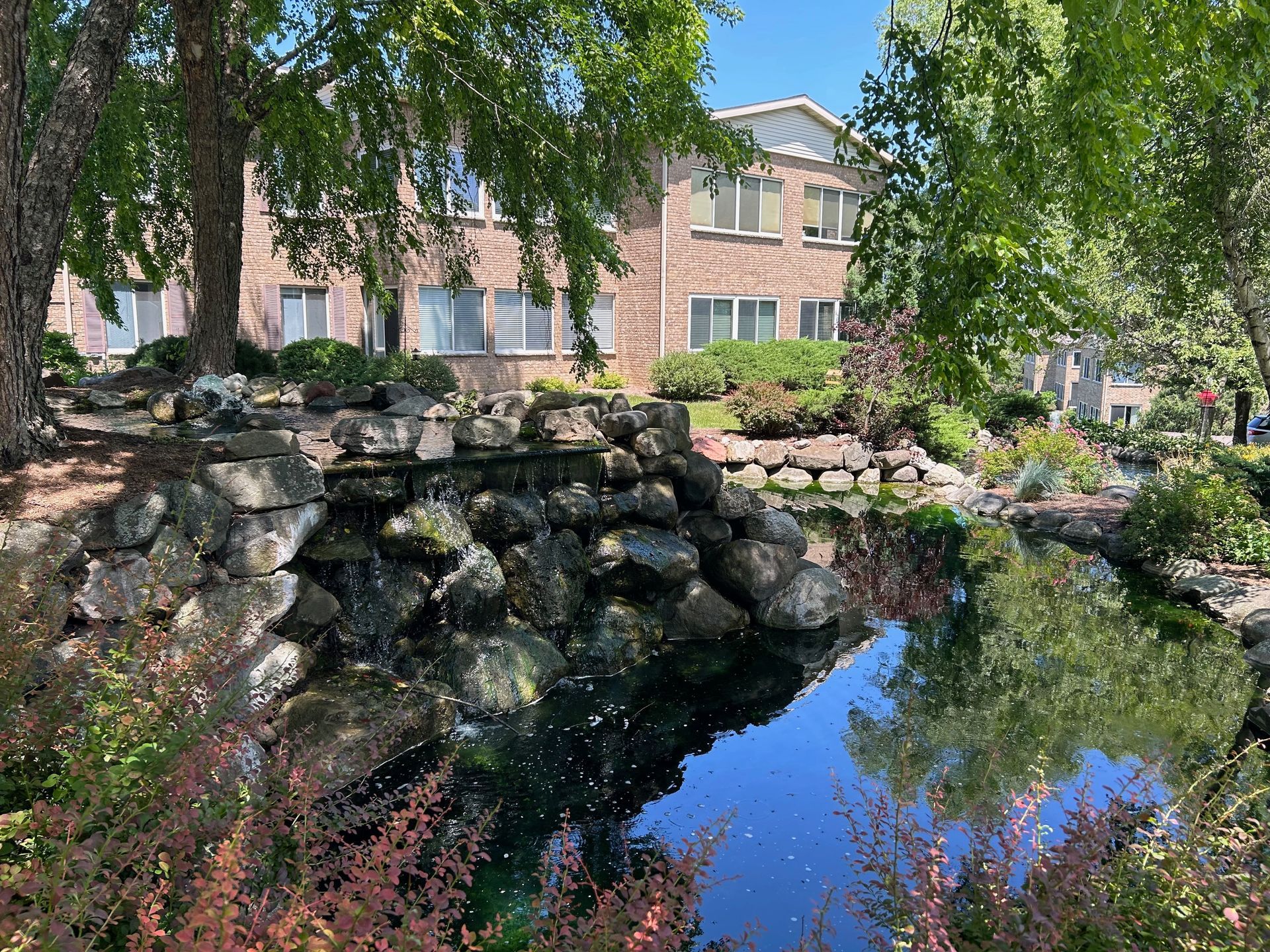 There is a pond in front of a building with a bridge over it.