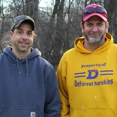 Two men are standing next to each other wearing hoodies that say property of deforest norskies