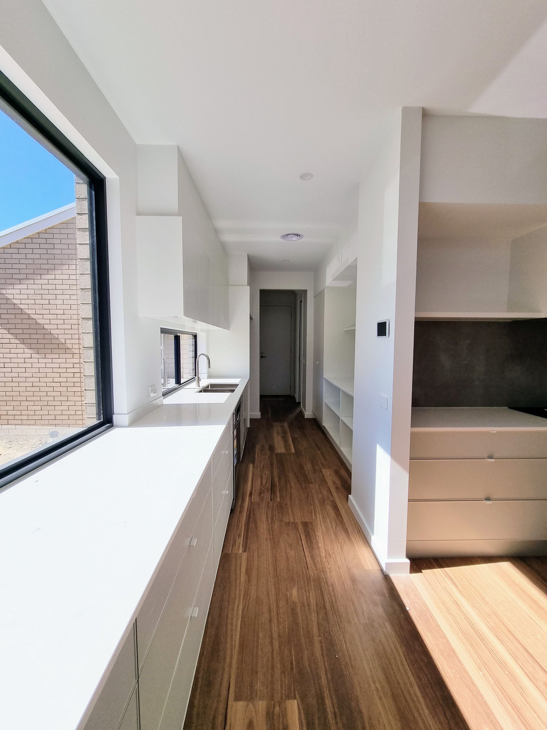 Long, narrow kitchen with wood floor, white cabinets and countertops, and a large window — Crampton Painting & Decorating Pty Ltd In Maiden Gully, VIC