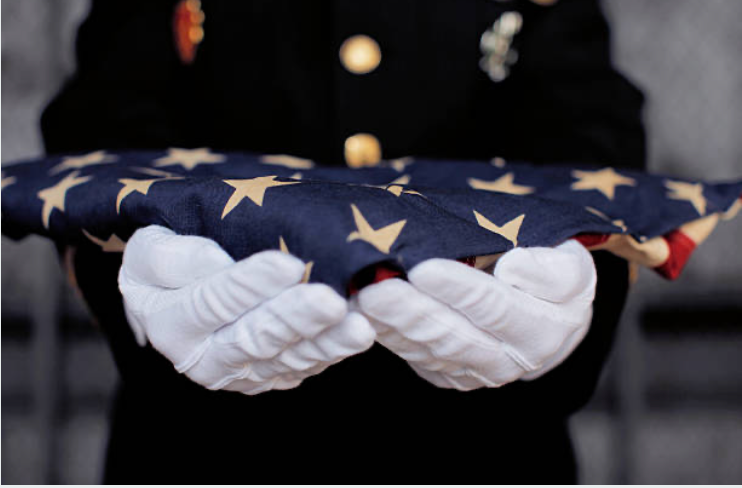 A man in a military uniform is holding an american flag in his hands.