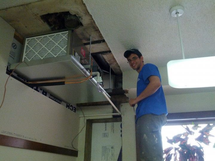 A man in a blue shirt is working on an air duct