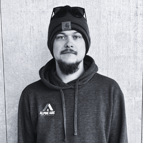 A man with a beard is wearing a black shirt and smiling in a black and white photo.