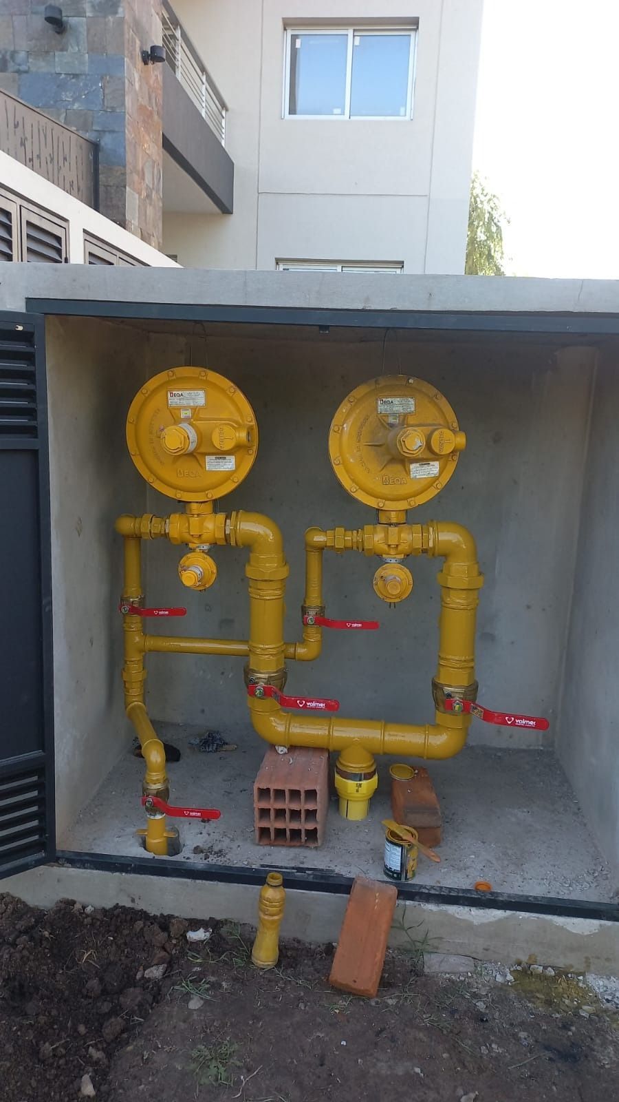 Sistema de medidor de gas de color amarillo en recinto de concreto, con válvulas y tuberías.