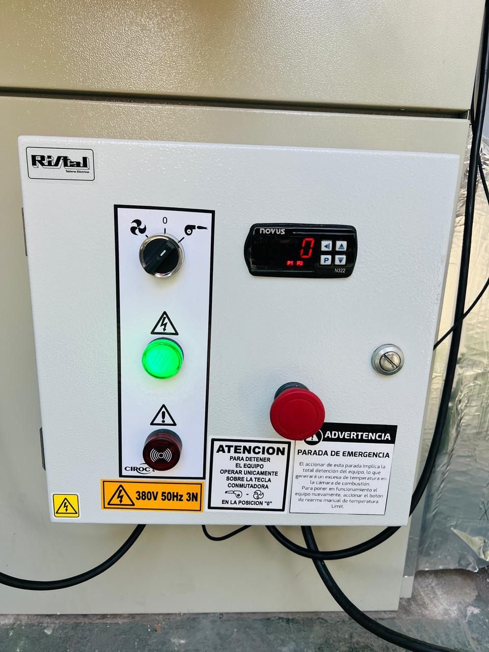Panel de control con perilla negra, luz verde, botón rojo y pantalla digital sobre una superficie gris.