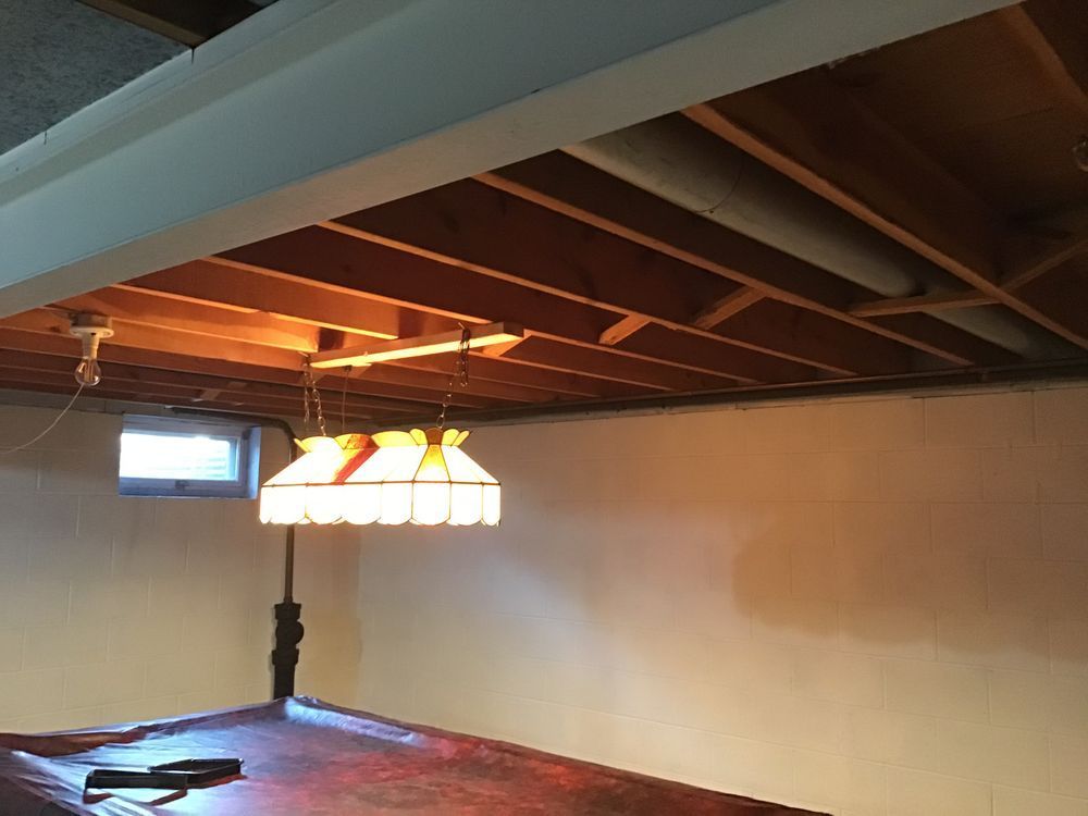 A pool table in a basement with a light hanging from the ceiling
