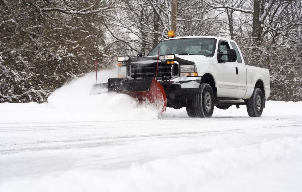 A white truck is plowing snow on a snowy road