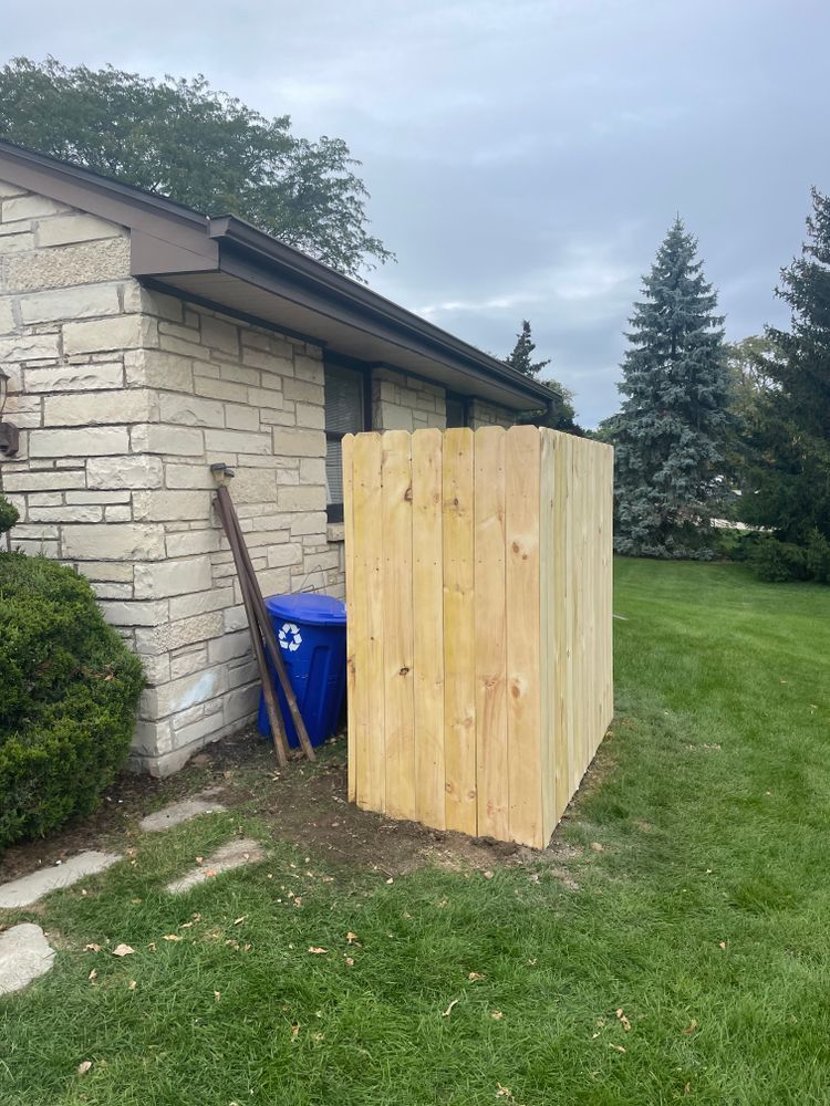 A wooden fence is sitting in the grass in front of a brick house