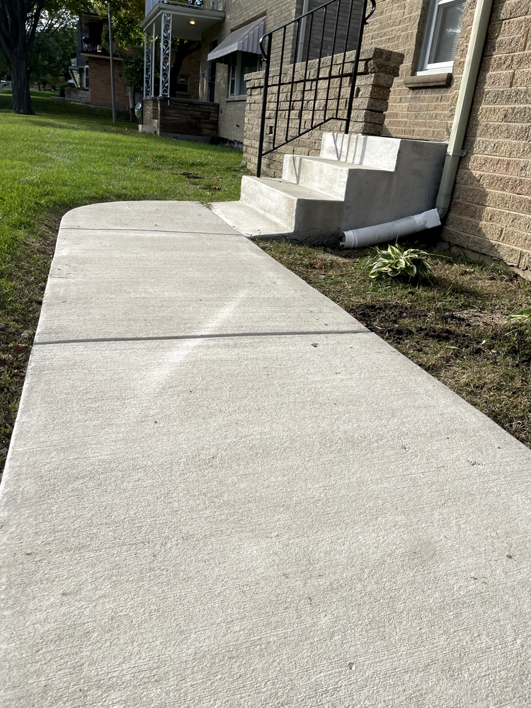 A concrete sidewalk next to a brick building with stairs