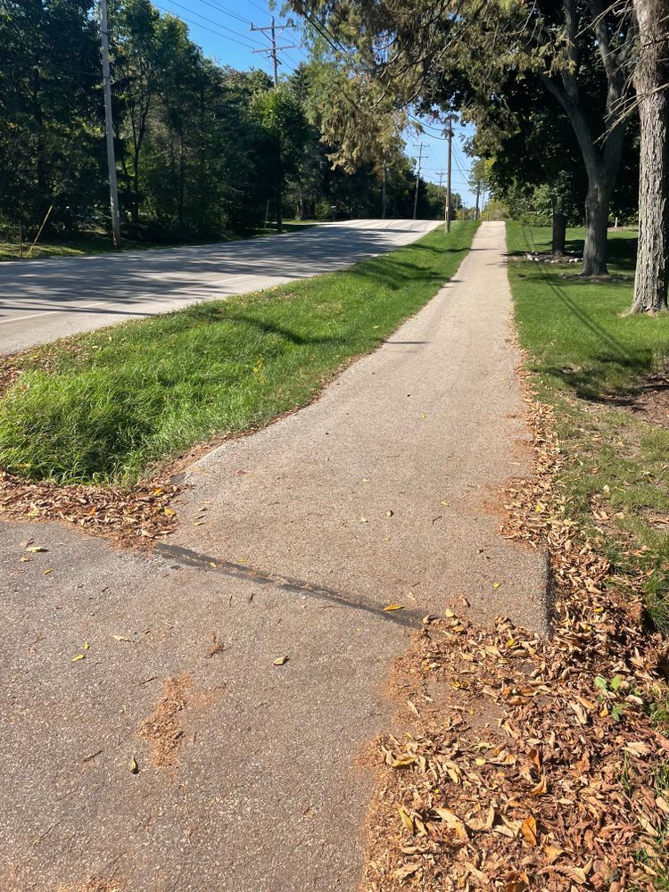 A sidewalk with leaves on the ground next to a road