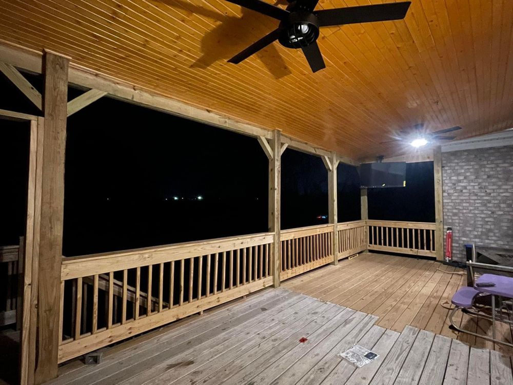 A large wooden porch with a ceiling fan at night