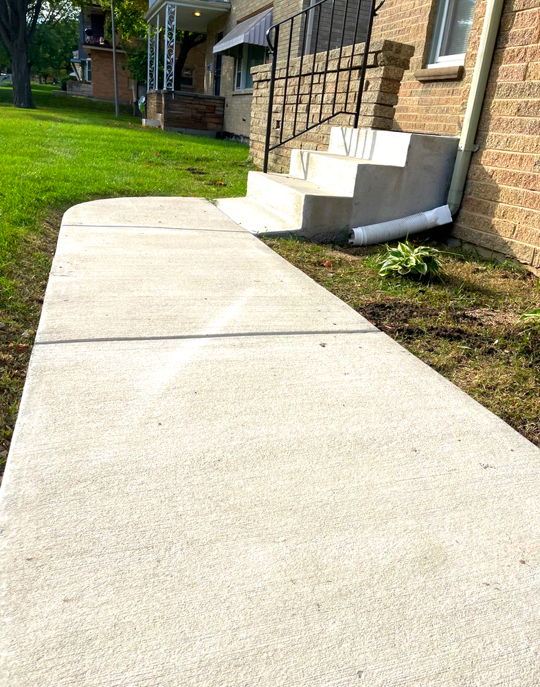 A concrete walkway leading to a brick house with stairs