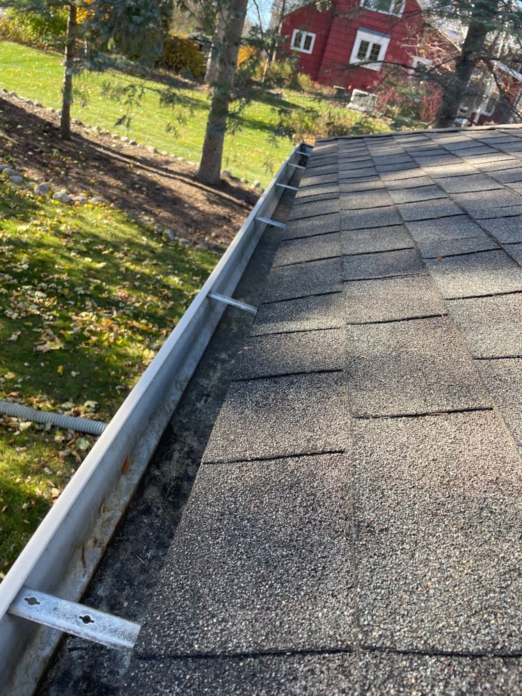 A close up of a gutter on a roof with a red house in the background