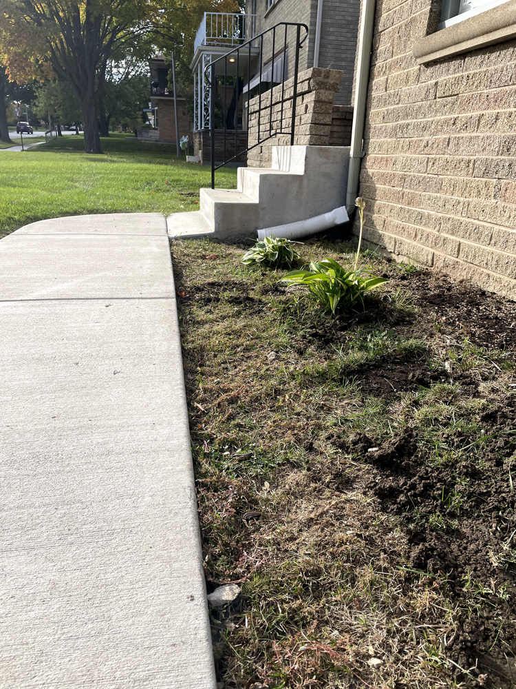 A sidewalk next to a brick building with stairs leading up to it