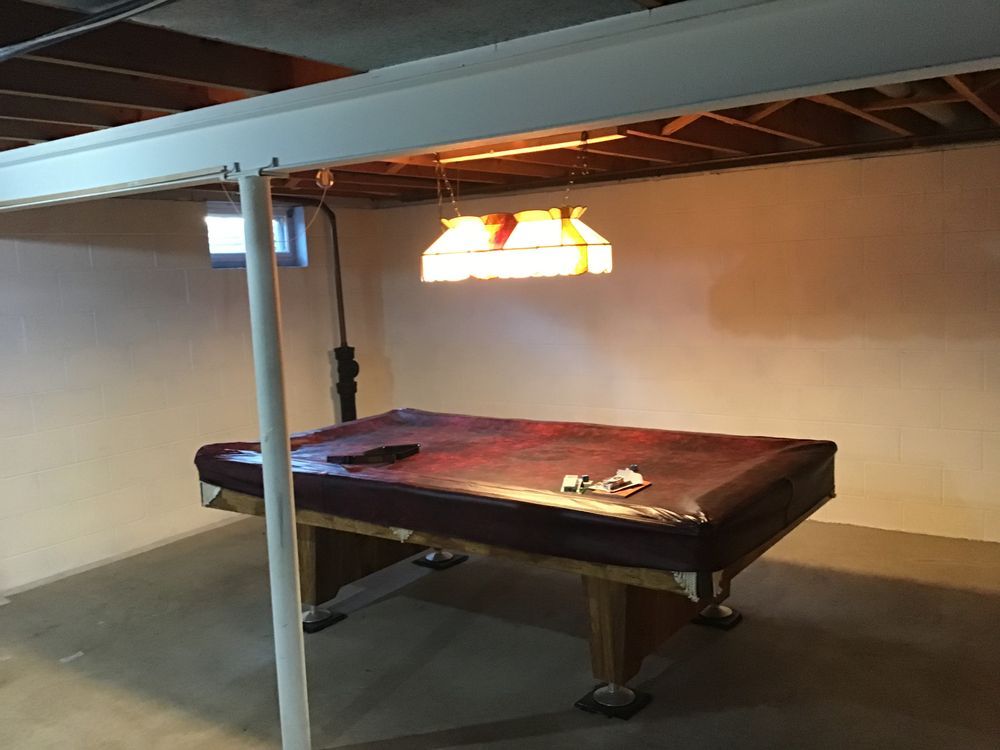 A pool table in a basement with a light hanging from the ceiling
