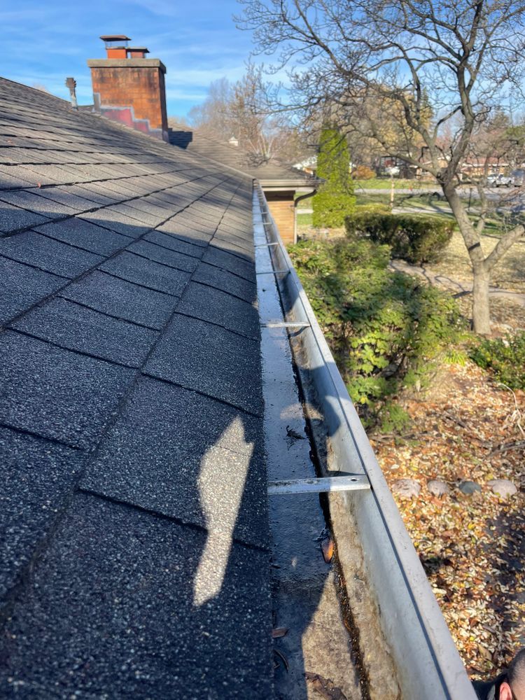 A gutter on the side of a roof with a chimney in the background
