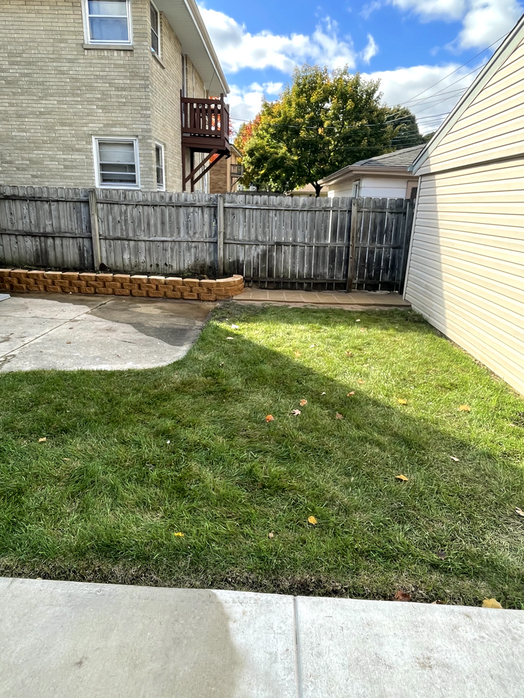 A backyard with a wooden fence and a house in the background
