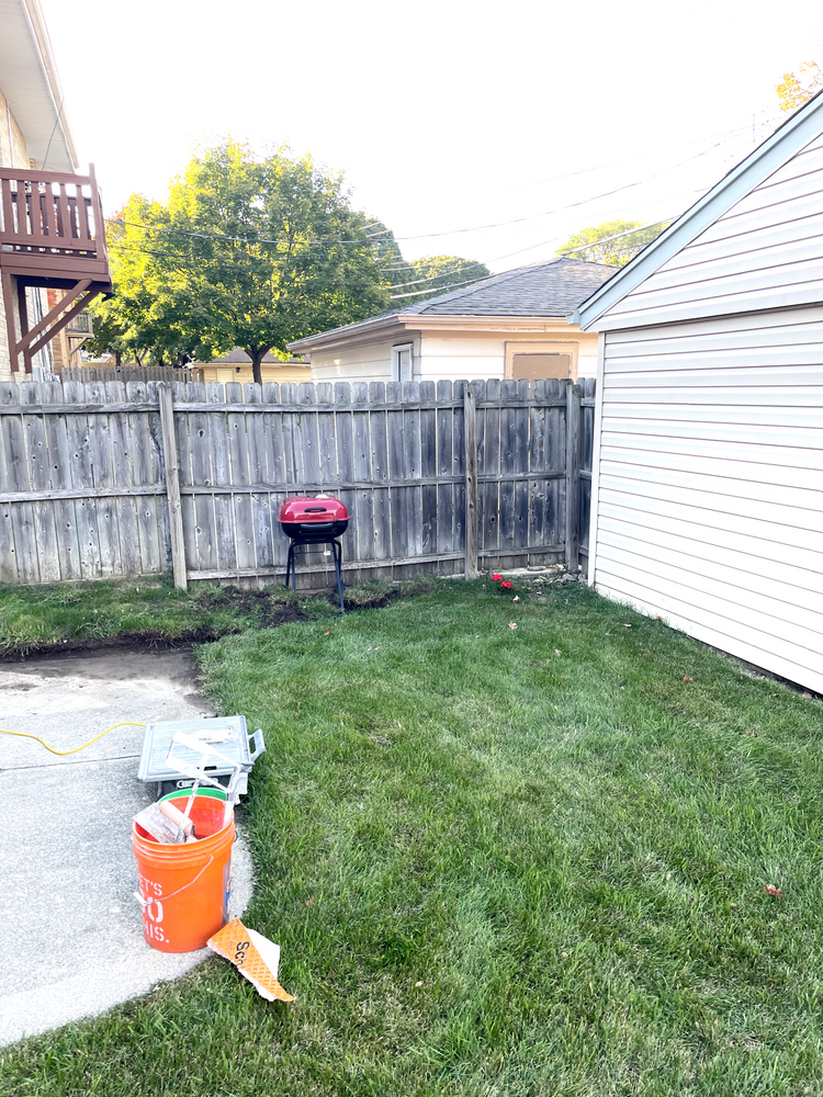 A backyard with a fence , a bucket , and a grill