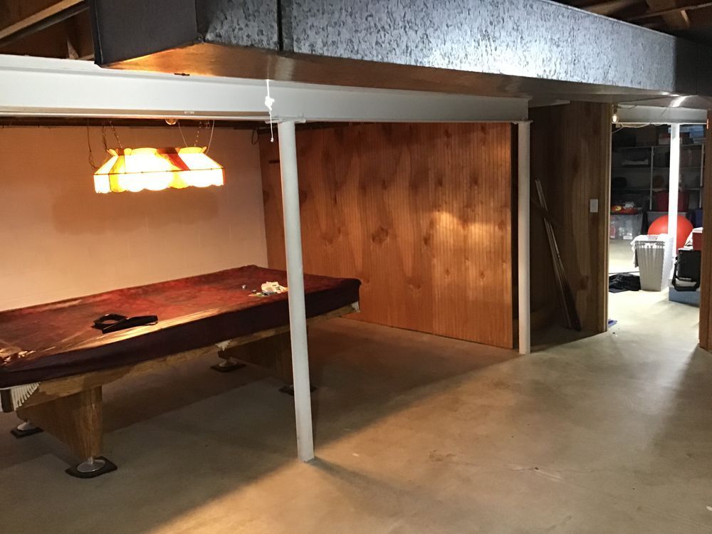 A pool table in a basement with a light hanging from the ceiling