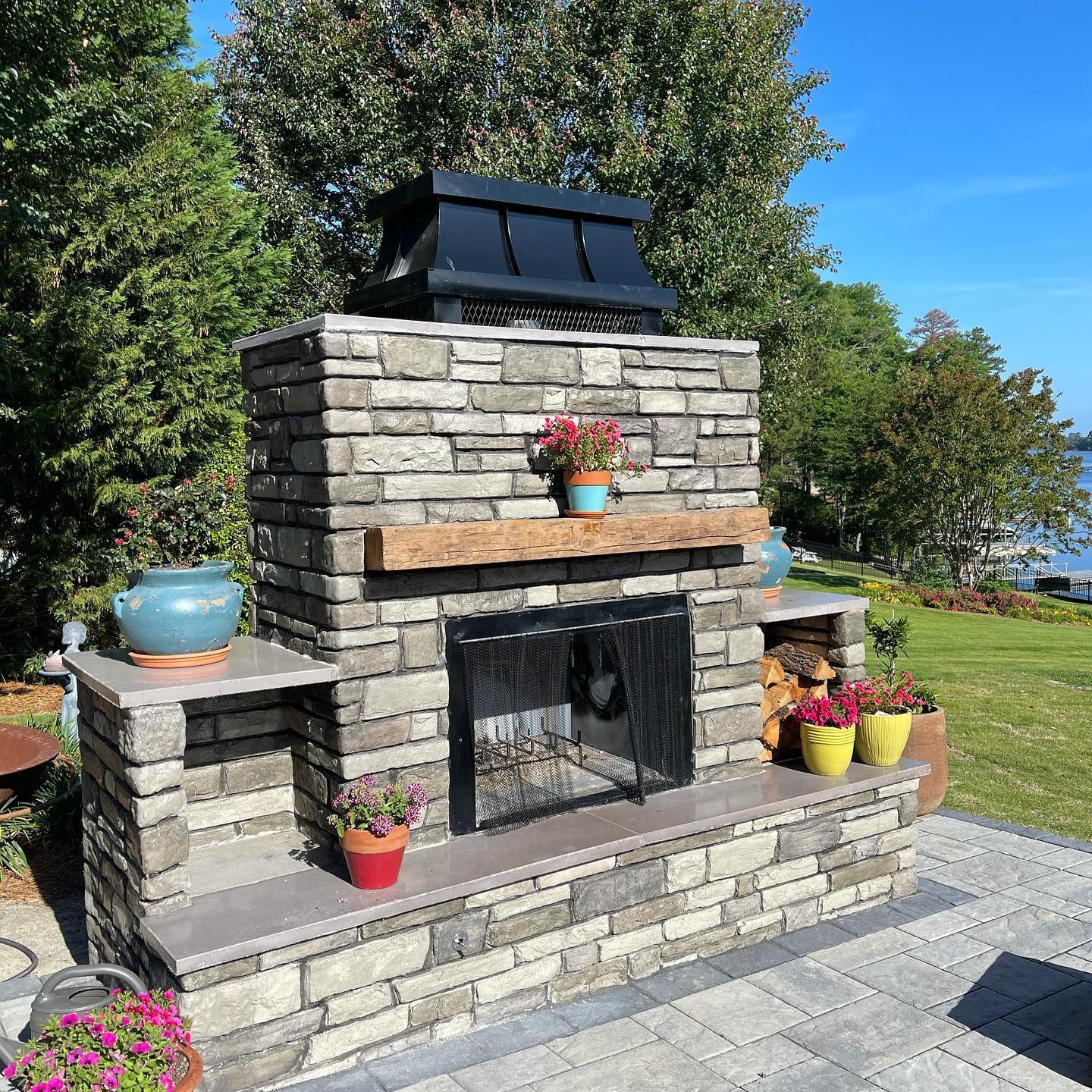 A brick fireplace with flowers and potted plants on a patio.
