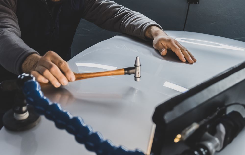 A Man is Using a Hammer to Fix a Dent on a Car — Smash Repairs In Harrington, NSW