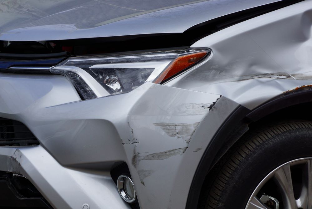 A Silver Car With a Damaged Bumper is Parked on the Side of the Road — Smash Repairs In Harrington, NSW